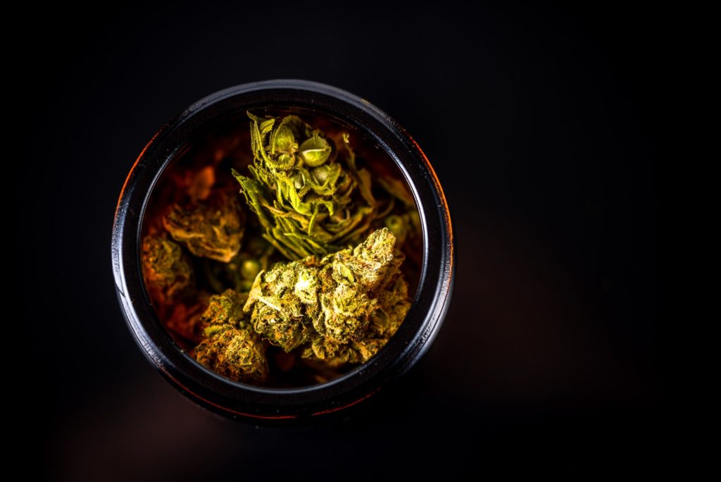 Cannabis Flower Buds in Glass Jar, Top Down Close Up. Dark Background. Medical Marijuana Concept